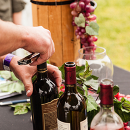 A person opening a wine bottle on a table with two other open wine bottles at LAWineFest photo courtesy After Image Studio