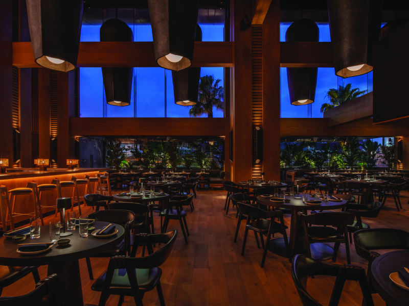 Interior dining photo of Katsuya, with elevated roof, wooden floor, wooden aesthetic. The redesign leans into minimalist Japanese elegance: ribbed wood columns, beam-lined ceilings, soft pendant lighting, and a stainless-steel sushi bar.